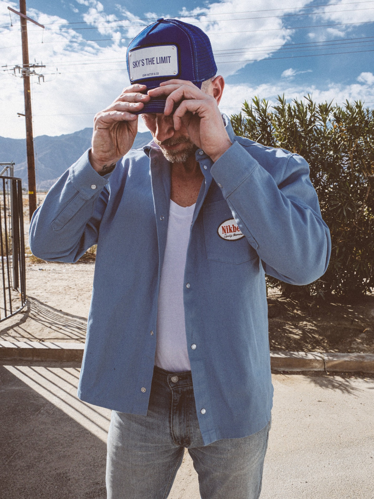 Man wearing a blue Sky's the Limit John Hatter trucker cap and blue shirt